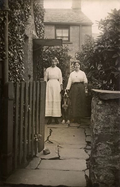 Two women with a dog outside a house