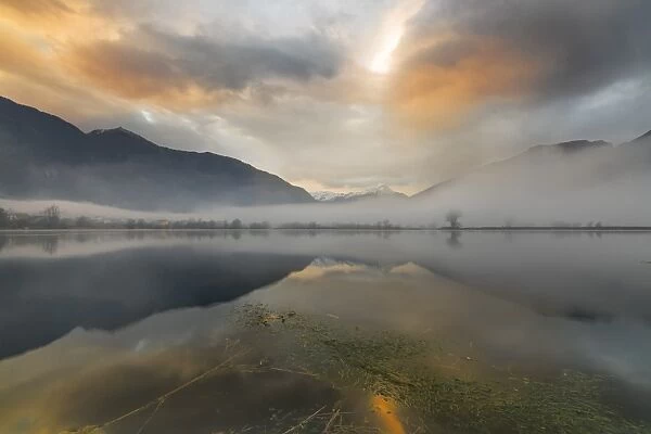 Mountains reflected in water at dawn shrouded by mist, Pozzo di Riva Novate, Mezzola