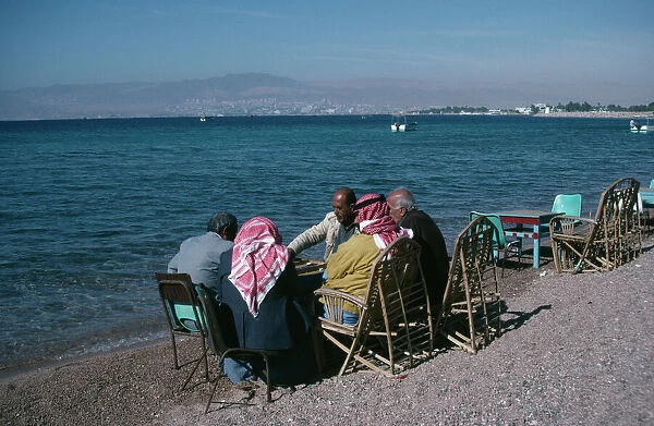 JORDAN, Aqaba Group of men playing backgammon on shore of beach with Eliat