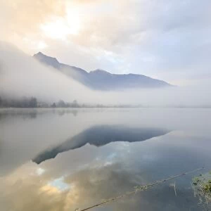 Mountains reflected in water at dawn shrouded by mist, Pozzo di Riva Novate, Mezzola