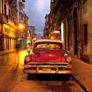 Red vintage American car parked on a floodlit street in Havana Centro at night, Havana, Cuba, West Indies, Central America
